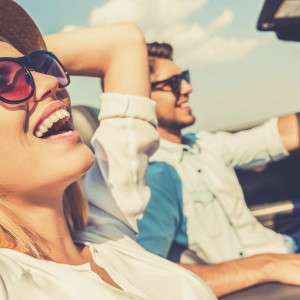 Freedom of the open road. Side view of joyful young woman relaxing on the front seat while her boyfriend sitting near and driving their convertible