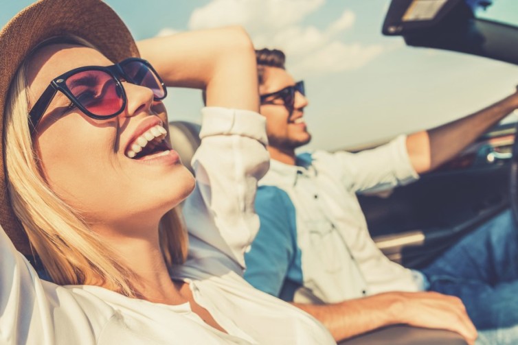 Freedom of the open road. Side view of joyful young woman relaxing on the front seat while her boyfriend sitting near and driving their convertible